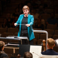 Conducting Fellow Juliane Gallant stands on the conducting podium, holding the baton between her two hands.