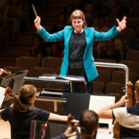 Conducting Fellow Juliane Gallant stands on the conducting podium, holding the baton in her right hand.