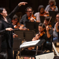 Conducting Fellow Monica Chen stands on the conducting podium.