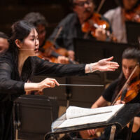 Conducting Fellow Monica Chen stands on the conducting podium.
