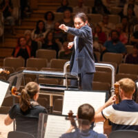 Conducting Fellow Kelly Lin stands on the conducting podium.